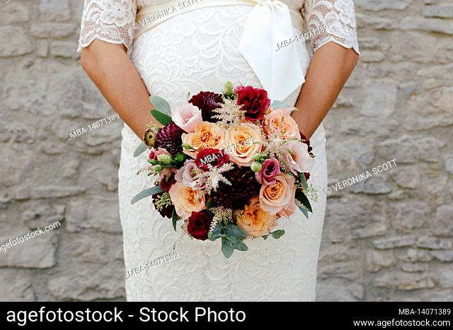 pregnant bride in a white lace dress with a colorful bridal bouquet in front of her belly