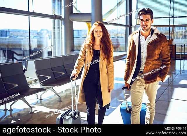 Confident business couple standing with luggage at airport departure area