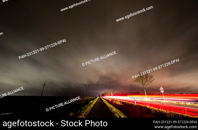 dpatop - 21 December 2023, Lower Saxony, Laatzen: Clouds pass over the Hanover region while cars drive along a country road (long exposure)