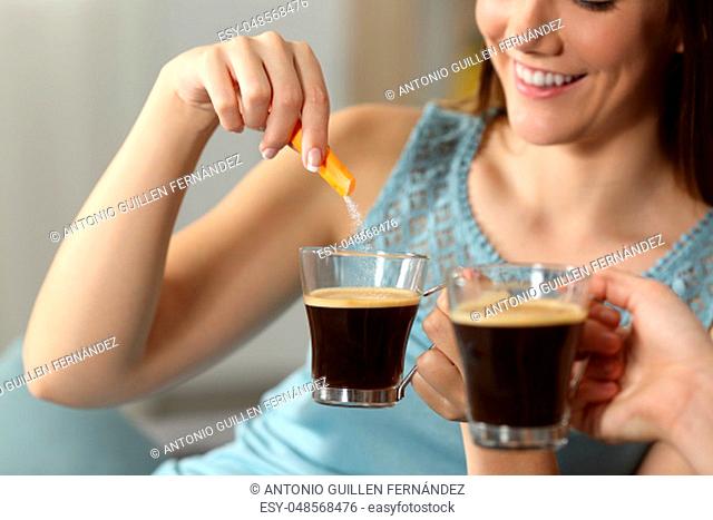 Close up of two women throwing sugar into coffee sitting on a couch in the living room at home