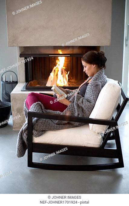 Young woman sitting in front of fireplace and reading
