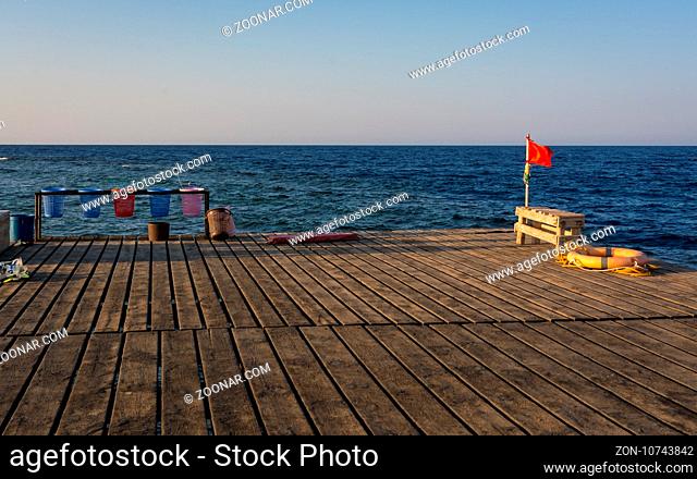 Red flag for warning lifebelt and colors baskets carry objects on a old wooden pier for diving and snorkeling at sunset.copy space