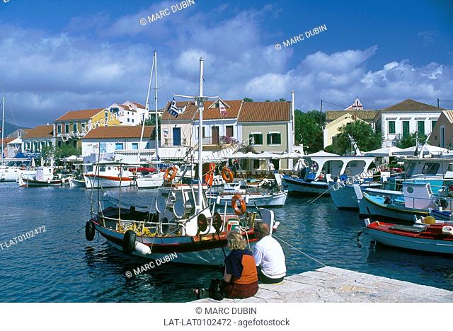 Ionian island. Cephallonia. Port. Boats moored. Houses. Two people sitting on wall