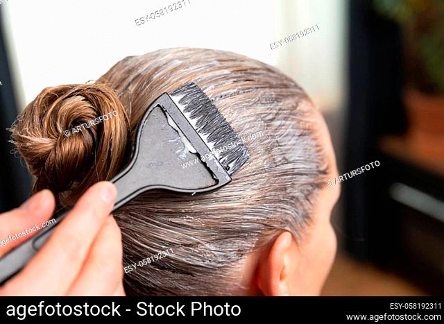 Hairdresser applying bleach or hair color for hair dye with a black brush at home or salon
