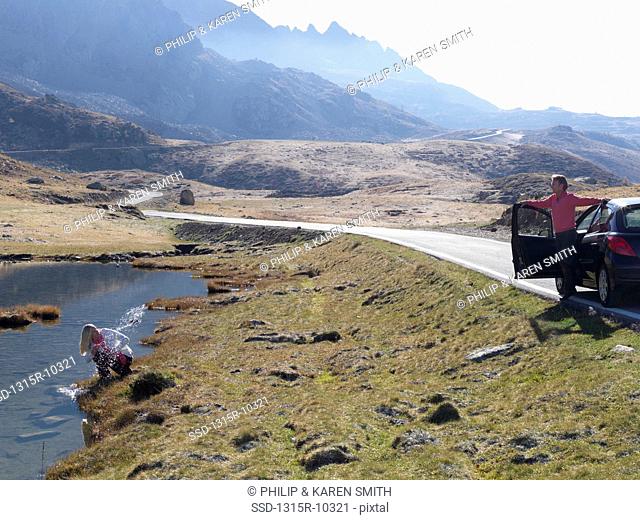 Italy, Piedmont, Woman splashing in mountain lake, man waiting