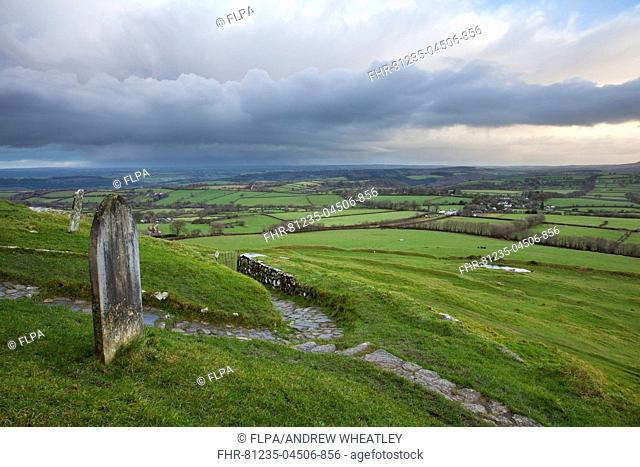 View of graveyard and path leading from 13th century church on moorland at sunrise, with rainclouds over distant countryside, Church of St
