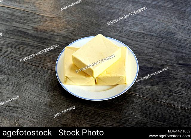 ayurvedic diet, steps to prepare homemade ghee from butter - three pieces of organic sour cream butter on a white porcelain plate, on a dark wooden tabletop