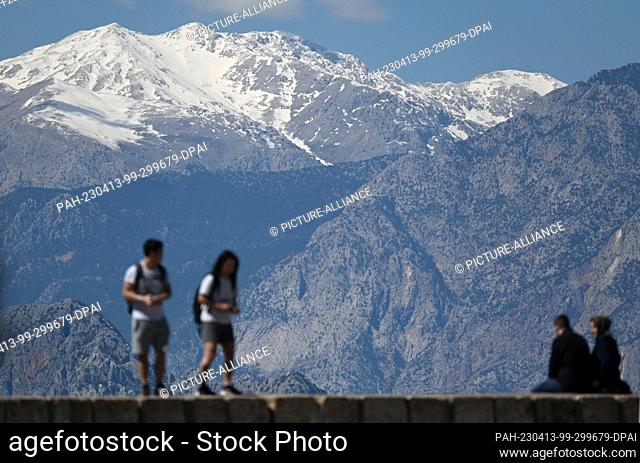 13 April 2023, Turkey, Antalya: Tourists stand on a wall of the Old Port of Antalya in front of snow-capped mountain peaks. Photo: Marijan Murat/dpa