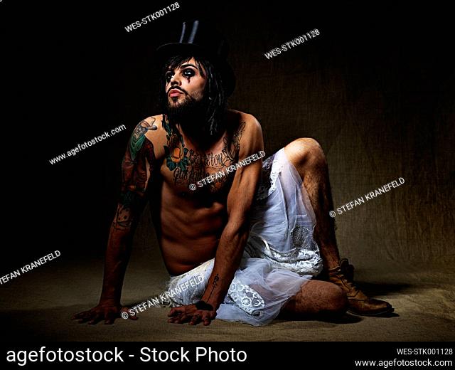 Portrait of man with full beard and eye make up wearing top hat and totu