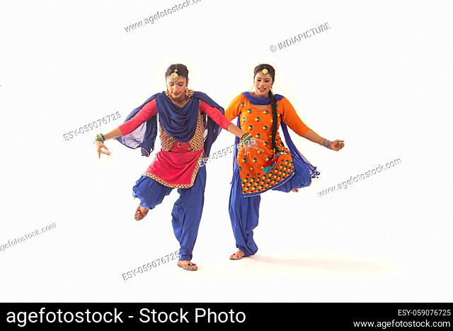 Two Giddha Dancers performing a dance step with hands stretched and a leg lifted up