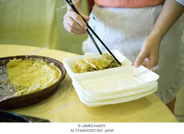 Food service personnel using chopsticks to place food in polystyrene container