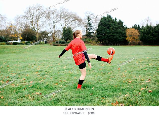 Teenage female soccer player practicing keepy uppy in park