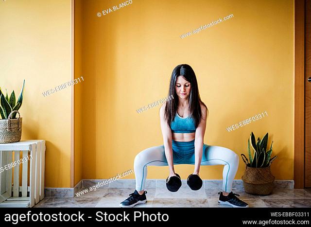 Sportswoman exercising with dumbbell in front of wall at home
