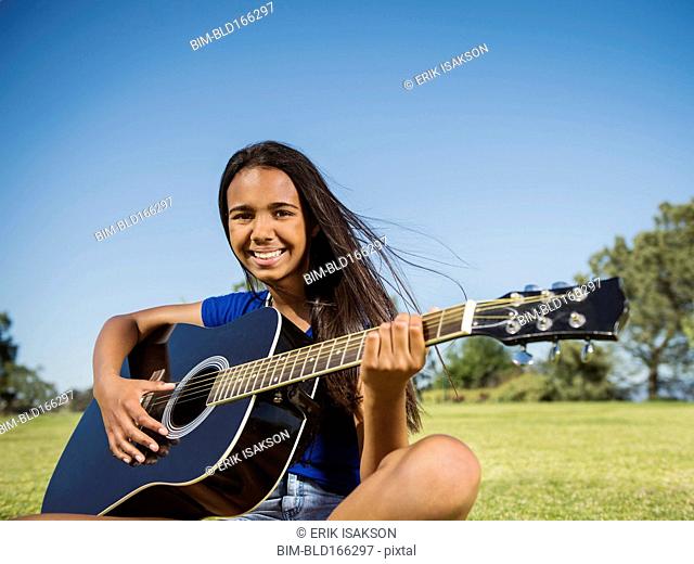 Mixed race girl playing guitar in park