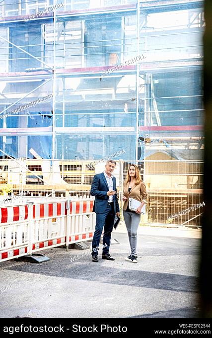 Building contractor examining construction site with businesswoman while standing against building