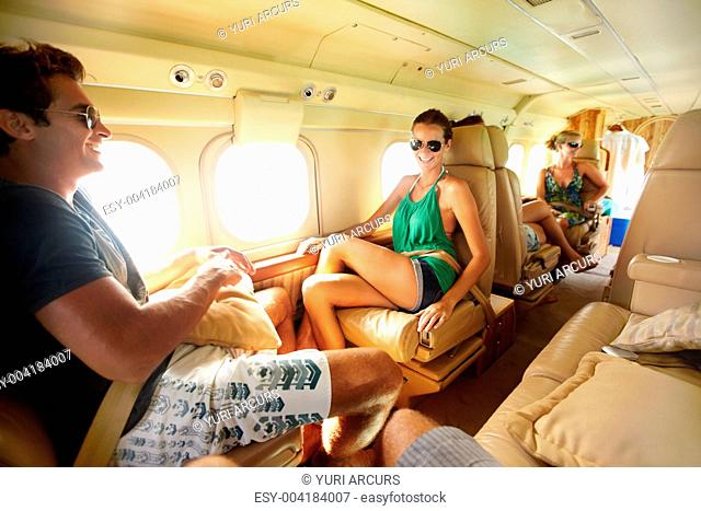 Happy young group of trendy friends sitting in a small aeroplane as the sun shines in throught the windows