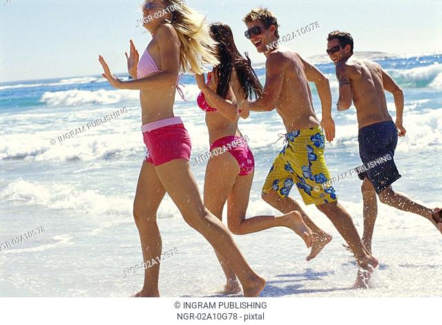 Two young couples running on the beach