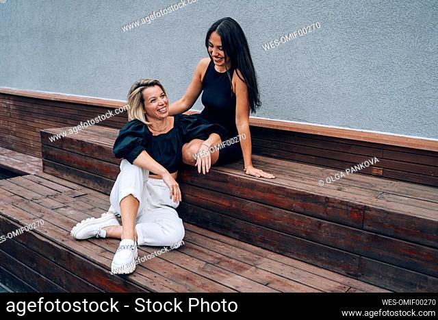 Happy friends sitting on wooden bench near wall