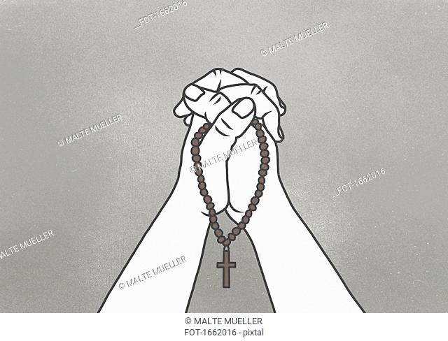 Cropped image of clasped hands holding rosary beads against gray background