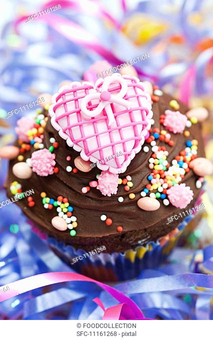 A chocolate cupcake topped with a pink heart for a party
