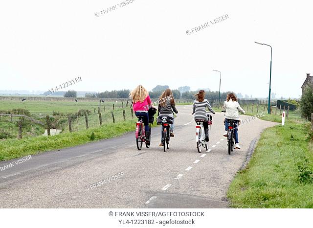 Girls biking side by side on the dike, going home after school, Netherlands