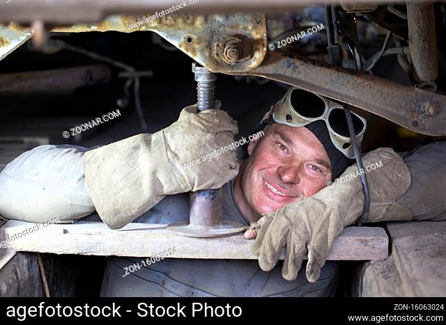 A male auto mechanic repairs a car in a garage.A man repairs a car body