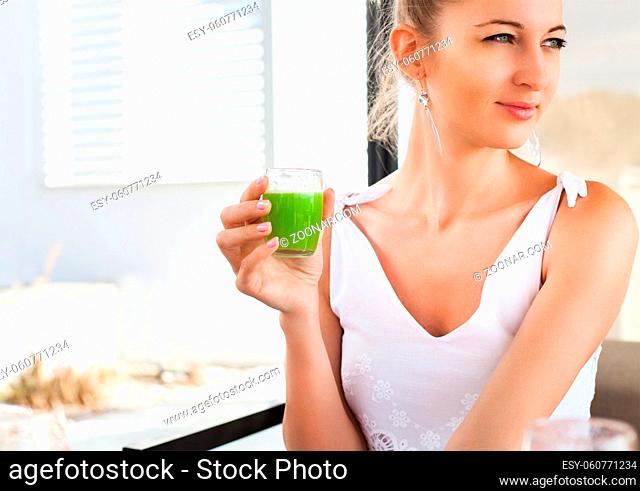 Woman holding glass of a green juice in her hand hand while having breakfast in the morning