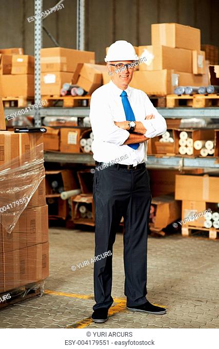 Portrait of a smiling male supervisor standing in a warehouse of stock crossing his arms