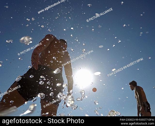 23 August 2023, Spain, Palma: People playing with a ball by the sea on a warm summer day at Cala Major beach. Spain is experiencing the fourth official heat...