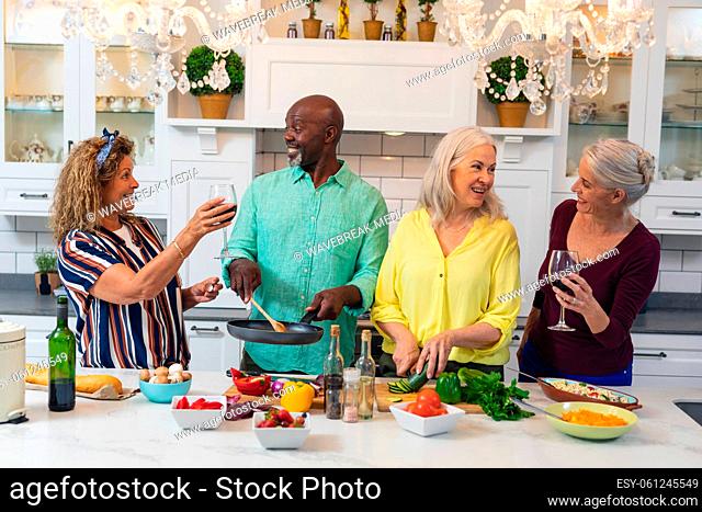 Happy caucasian senior women having wine while friends preparing food together at home