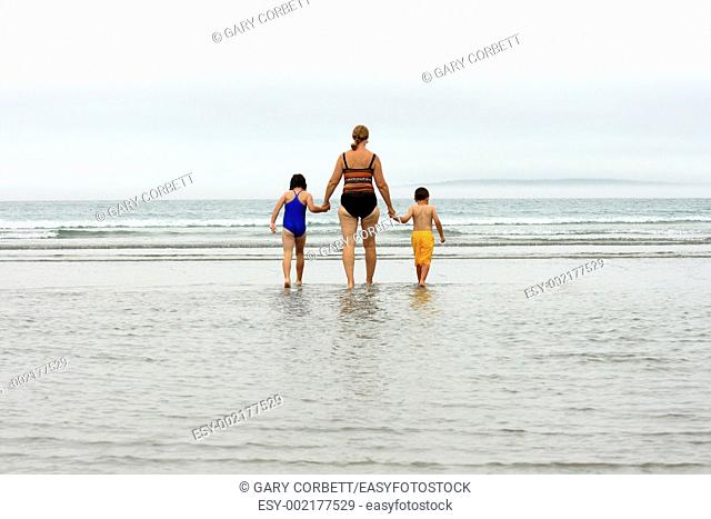 a grandmother walking into water at beach with two children in hands