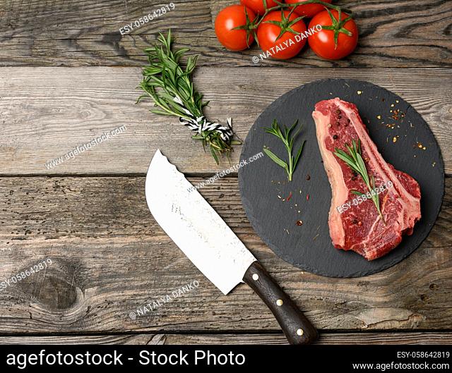 fresh piece of beef, striploin steak on a black board with spices, top view