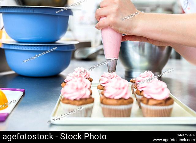 Women in pastry bakery as confectioner glazing muffins with icing bag, close-up