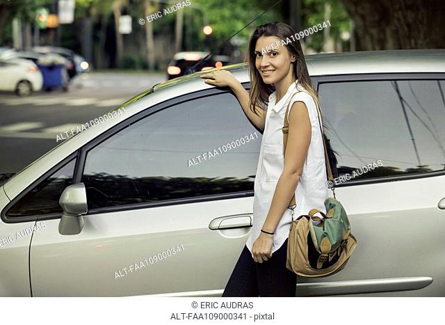 Young woman leaning against car, smiling