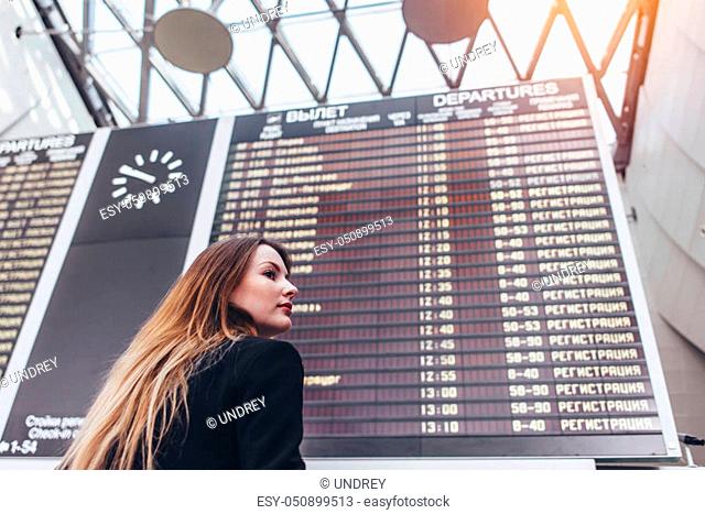 Young woman standing against flight timetable in airport