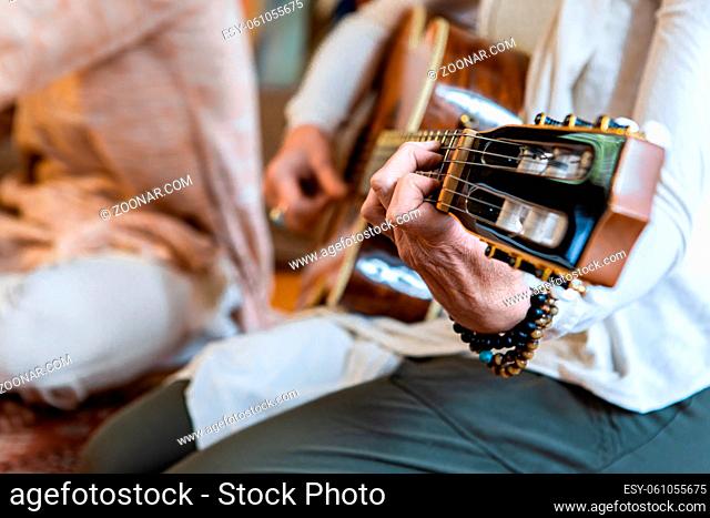 Selective focus of woman hand playing classical guitar having nylon strings with sacred music tone for meditation while sitting on floor carpet