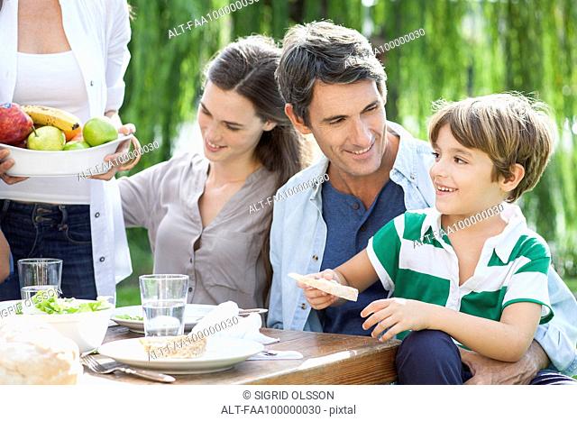 Family eating together outdoors, father holding son on lap