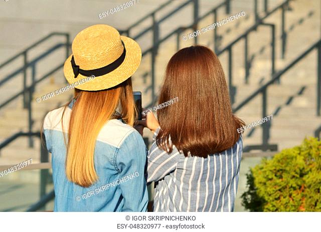 Two young girl friends take a selfie walking on the street in the city Park