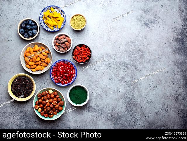 Set of different superfoods in bowls on stone gray background: spirulina, goji berry, cocoa, matcha green tea, quinoa, chia seeds, blueberries