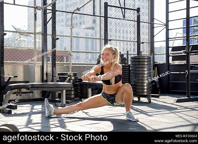 Smiling woman doing stretching exercise at rooftop gym
