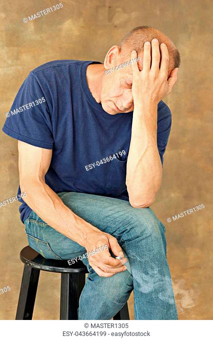Worried mature man sitting at studio, smoking and thinking about something