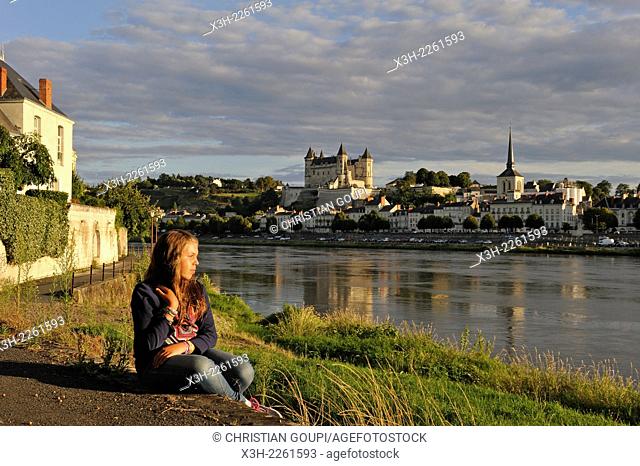 young girl sitting on Loire River bank with the Chateau de Saumur in the background, Maine-et-Loire department, Pays de la Loire region, France, Europe