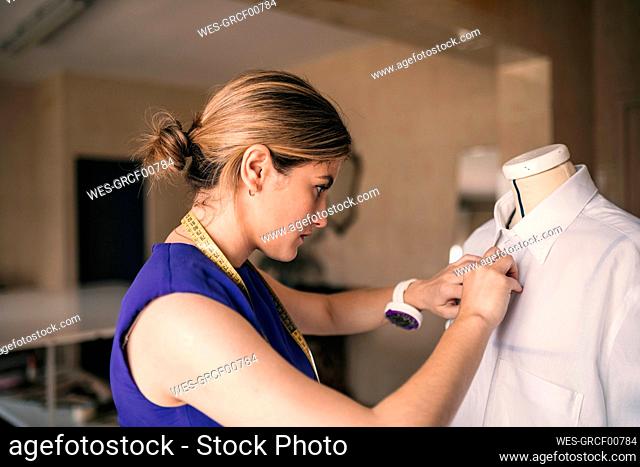 Female fashion designer buttoning mannequin shirt at workshop