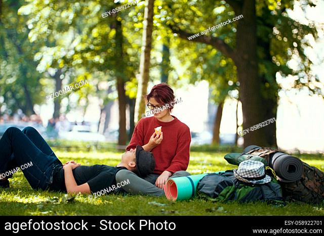Couple of teenagers tourists with backpacks have rest in the city park, telephoto shot