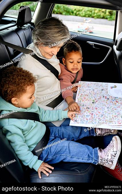 Senior woman reading book with children in car
