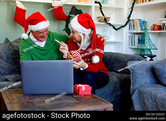 Senior couple in santa hat sitting on couch holding gift box and smiling looking at each other while