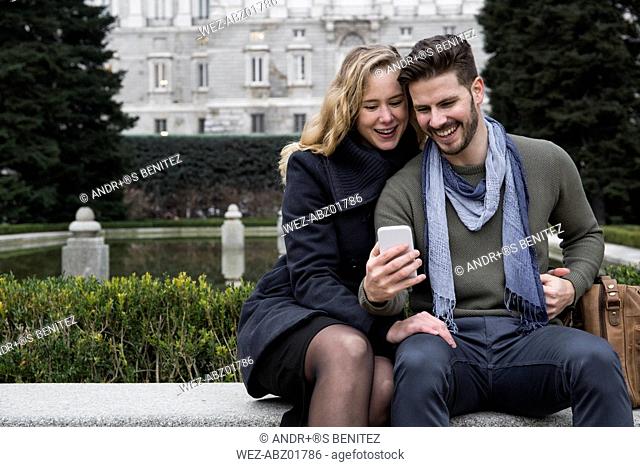 Spain, Madrid, happy couple with cell phone with the Royal Palace in background
