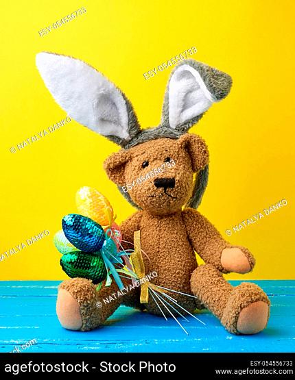 vintage cute brown teddy bear holding colorful Easter eggs, wearing a rabbit mask with long ears on his head, funny holiday card