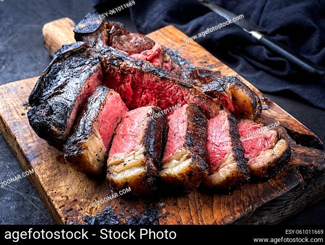 Traditional barbecue dry aged wagyu t-bone beef steak bistecca alla Fiorentina sliced and served with black salt as close-up on an old rustic wooden board