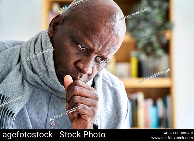 Visibly ill man of African-American ethnicity coughing in his hand